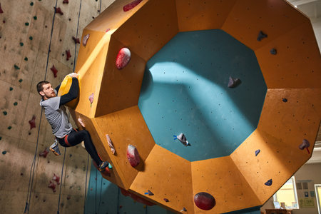 Physically impaired male mountaineer trains indoors at bouldering gym, climbing difficult round-shaped wall, has athletic muscular body shape, ambitious and motivated person.の写真素材