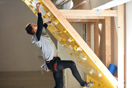 Side view of young male rock climber with physically disability starting bouldering training at...