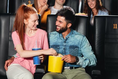 Happy cheerful couple sitting in movie theater, watching movie, eating popcorn, enjoying pastime. happiness, unforgettable moments. love. warm, tender feeling and emotionの写真素材