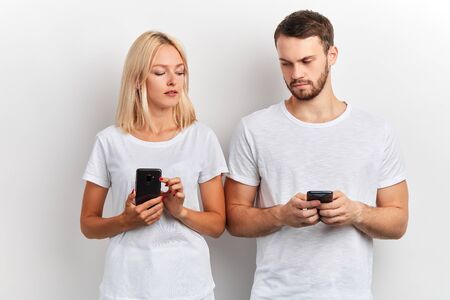 two attractive people comparing their smart phones, close up portrait, isolated white background, studio shotの写真素材
