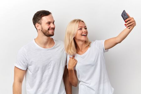 positive young man and woman taking photo of themselves, leisure, pastime, isolated white background, studio shotの写真素材