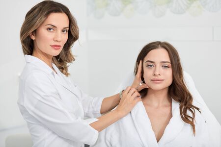 beautiful woman in white bathrobe sitting in the clinic and getting anti-aging, anti-wrinkle injection. close up portrait, lifestyle, job, profession, occupationの写真素材