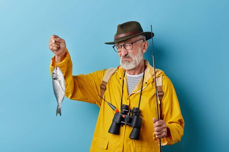 unhappy depressed old man being upset with bad day for fishing, negative feeling and emotion. close up photo. isolated blue bacakground, depressionの写真素材