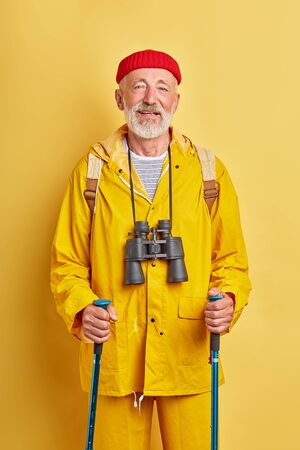 old tourist with binocular in stylish coat takes care of health, wellness, fitness, treatment. close up photo. isolated yellow backgroundの写真素材