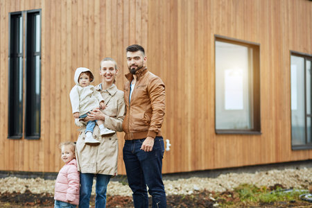 Family of four stand on front house, pose and look at camera.