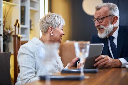 Beautiful senior couple spending time together in rich restaurant look at gadget, smile, cheerfulの写真素材