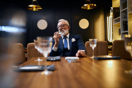 Senior grey-haired man holding and smoke e-cigarette in rich restaurant . IQOS, modern technologies,...