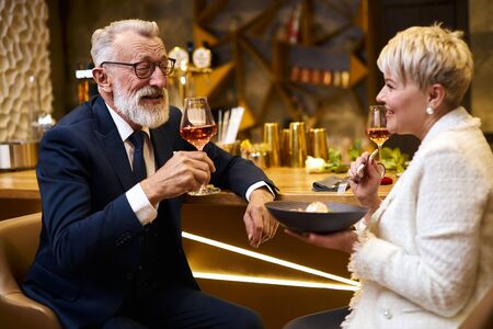 Caucasian man in suit and eyeglasses, beautiful woman in white elegant blazer enjoy meal in attractive place. Sweet dessert and glass of champagne. Love in the airの写真素材