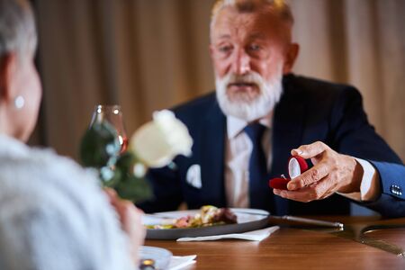 Caucasian gray-haired man in tuxedo offers to get married. Lovely face of male. Woman keep white rose in handsの写真素材