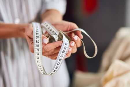 womans hand holding tailor measuring tape. close up cropped photo. tailors equipmentの写真素材
