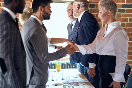 Group of businessmen at table in office shaking hands.