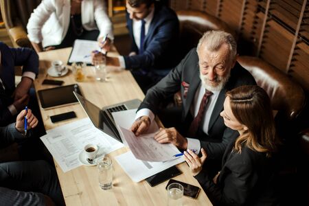 Couple of sociable business partners sitting on comfortable brown leather sofa, solving business problems at conference in bright lighted office, on the background of brown jalousie Close upの写真素材