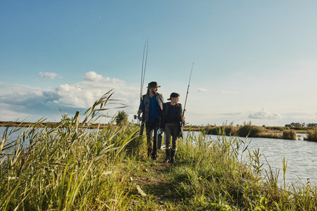 Caucasian father and son walk on islet among lake. They choose good place for fishing together to get big catch and then cook on fireの写真素材
