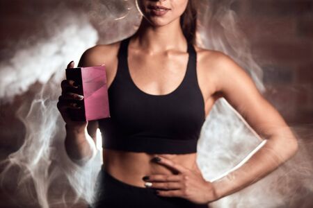 Fit woman in sport topic holding sport nutrition, food in box standing in steam background. Sport, crossfit, bodybuilding, healthy lifestyle conceptの写真素材