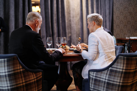 Backs of restaurant visitors, sitting in soft comfortable armchairs, eating well prepared meal,...