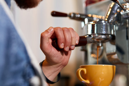 Hand of male barista with plaster on finger, keeps tamper on coffee machine, presses hot tasty...