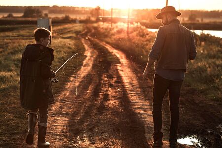 Father and son walk along country road along lake to fishing spot. Sunset.の写真素材