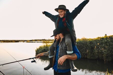 Father and son have fun while fishing. Teen boy happy and smile, sit on father shoulders and raised hands to sides.の写真素材