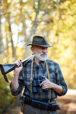 Portrait of senior bearded huner holding shotgun, using binocular while hunting on wild animals, look awayの写真素材
