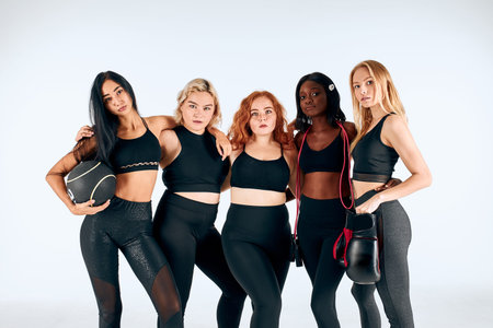 Slim attractive young girls stand together isolated over white background, with balls, dumbbells, healthy and sportiveの写真素材