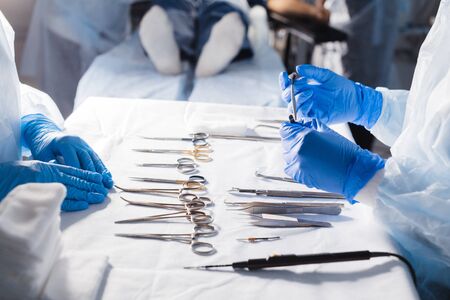 Detail shot of steralized surgery instruments with a hand in surgical gloves taking a tool with art lighting and blue filter, close upの写真素材