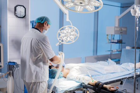 Assistant holds mask and induction for general anesthesia over patient head, getting ready to...