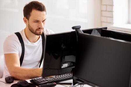 Handsome busy man working on computer, look at screen of computer. Office background