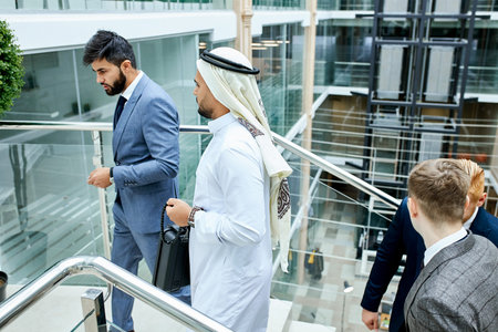 Caucasian man in tuxedo and sheikh go up the stairs and speak, discuss future business ideas