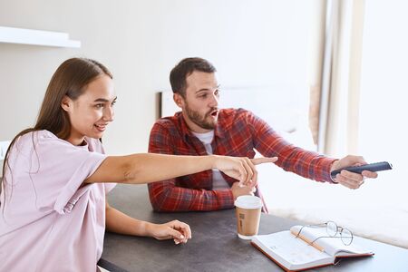 Happy excited man and woman choosing good film to watch, pointing with finger at tv set, sitting comfortably at table, having rest, holiday concept, portraitの写真素材