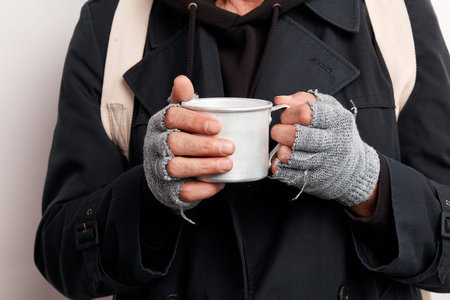 Homeless man wearing street clothes, unrecognizable. Beggar holding cup tea trying to warm up