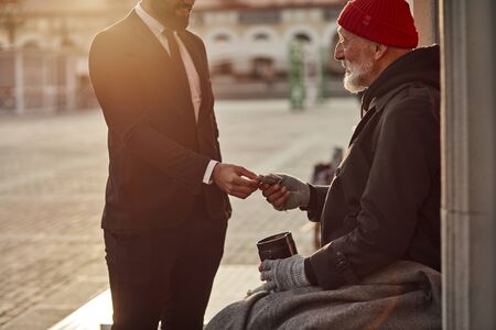 Homeless senior man hold out his hand to get money from unrecognizable rich man. Street lifeの写真素材