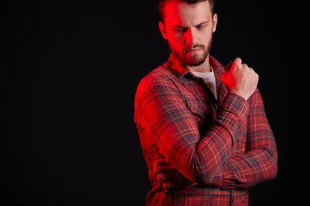 people concept. Young caucasian man with beard stand looking down, wearing red casual shirt. Isolated over black background, red neon light on himの写真素材