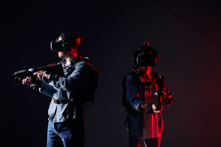 Couple of virtual reality gamers stand in neon backlit, back to back. Man and woman with virtual...