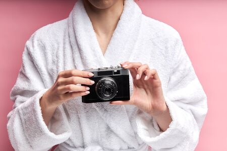 Closeup photo of woman hands holding photo camera and standing isolated over pink backgroundの写真素材