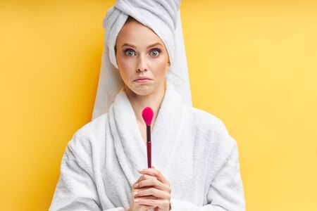 Confused caucasian woman in bathrobe and towel, look perplexed at make-up brushes.の写真素材