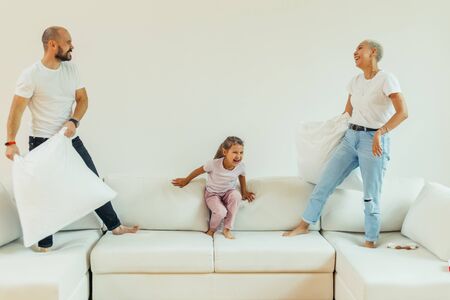 Happy joyful family fighting pillow battle on bed at home with children. Positive family, laughing. Friendly familyの写真素材