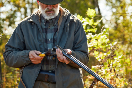 Senior hunter load rifle and going to shoot. Man in hunting casual clothes, autumn forest background
