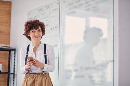 Beautiful caucasian woman using modern mobile phone during work in office, scheme board backgroundの写真素材
