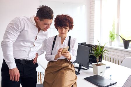 Caucasian co-workers stand together looking on smartphone, woman showing man information on smartphone screen.の写真素材