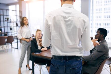 View on back of man in white shirt speaking with international group of business peopleの写真素材