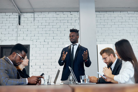 Personable black employee explains to foreign colleagues new client management strategy idea at...