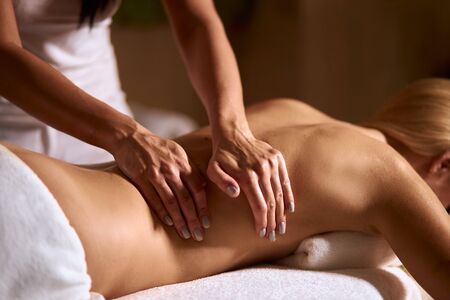 Young blonde woman in wellness beauty spa having aroma therapy massage with essential oil, gentle female hands massaging back of client, total relaxation, close upの写真素材