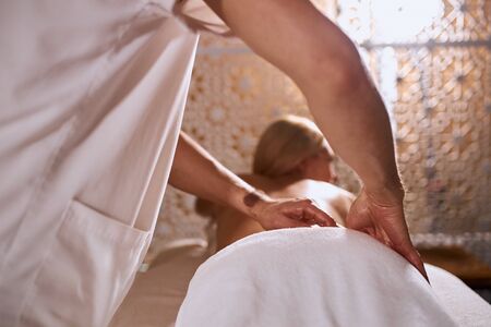 Low angle shot of hand massage process, male hands of professional physiotherapist massaging body of young woman in beauty treatment spa salon, indoor shotの写真素材