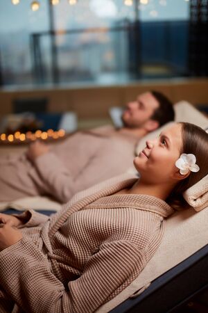 Young caucasian couple relax on loungers in spa center, taking rest together, lying around candlesの写真素材