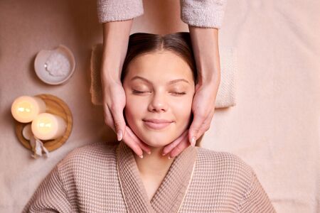 High angle view on pleased woman getting massage in spa salon, candles near herの写真素材
