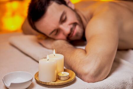 Handsome caucasian lying after massage in the beauty salon, spa salon, naked skin. Young bearded man relaxing,yellow wall background in spaの写真素材