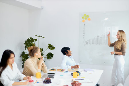 Young beautiful business coach teacher team leader represent her business strategy to co-workers in...