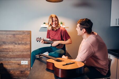 attractive young caucasian woman in casual wear playing ukulele for man listening to herの写真素材