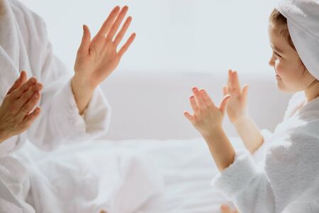 caucasian woman and little child daughter sit playing game of clapping hands together, friendly familyの写真素材