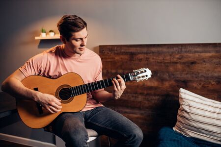 Portrait of young caucasian man playing the guitar at home, attentive careful music performer isolated over roomの写真素材